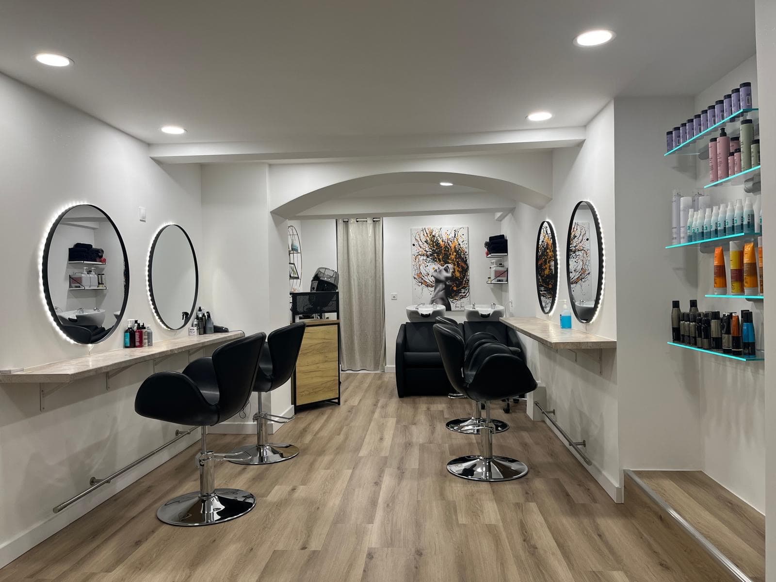 Intérieur du salon SSA Coiffure à Chêne-Bougeries : miroirs ronds lumineux, fauteuils design et parquet clair